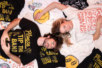 Two people lying on a bed of graphic t-shirts, wearing graphic t-shirts with text and graphics.