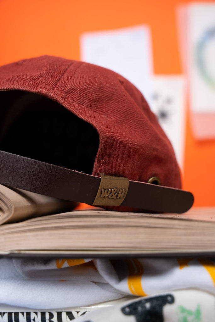 Red cap with a brown strap on top of a book against an orange background