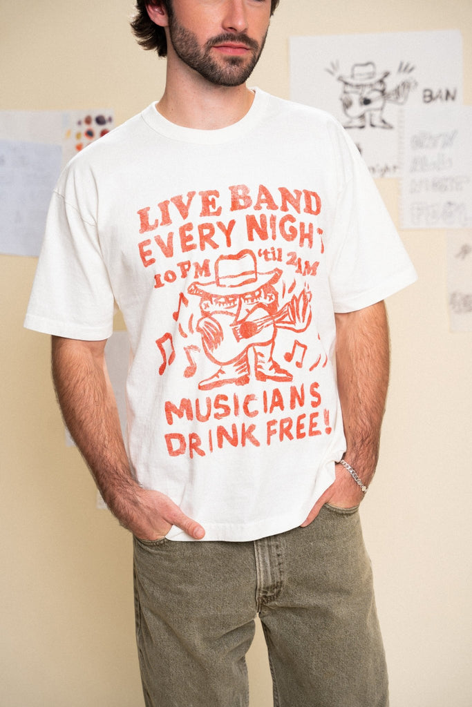 Man wearing a white t-shirt with red graphic and text that read "live band every night musicians drink free" standing against a cream background.