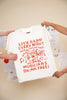 White t-shirt with red text and graphics that read "live band every night musicians drink free" held by two people against a light background