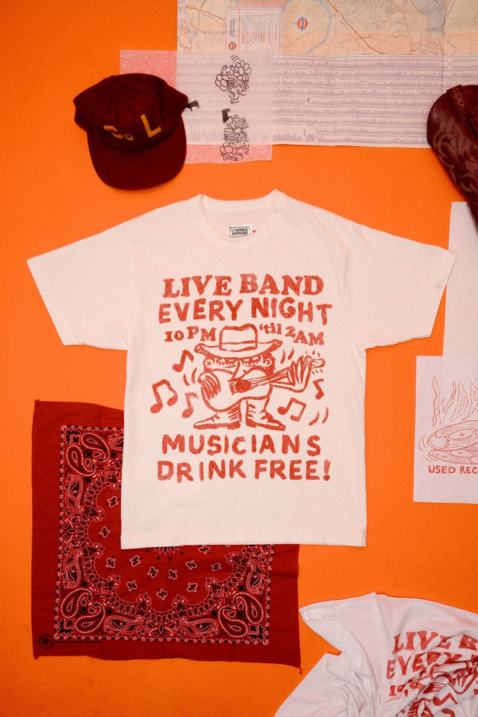 White t-shirt with red text and graphics that read "live band every night musicians drink free"on an orange background, accompanied by a bandana and another t-shirt.