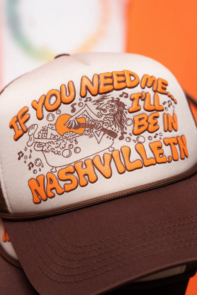 Cream and brown trucker hat with text 'If you need me, I'll be in Nashville, TN' on an orange background.