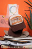 brown and white cap with text and graphics, that say "if you need me...I'll be in Nashville, TN" on a stack of books against an orange background