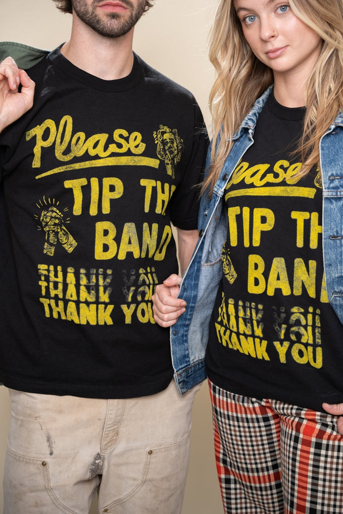 Two people wearing black t-shirts with yellow text that reads "please tip the band thank you"