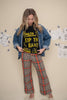 Woman wearing a denim jacket, black graphic t-shirt, and plaid pants against a wall with drawings.