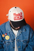 Person wearing a cap with text and a denim jacket against an orange background
