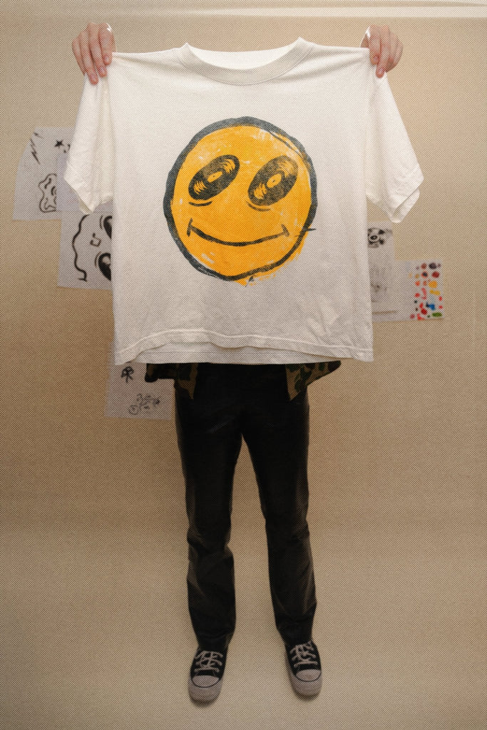 Person holding a white t-shirt with a smiley face design against a plain background