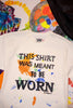 White sweatshirt with colorful text that says "this shirt was meant to be worn", and paint splashes, displayed against a colorful abstract background.